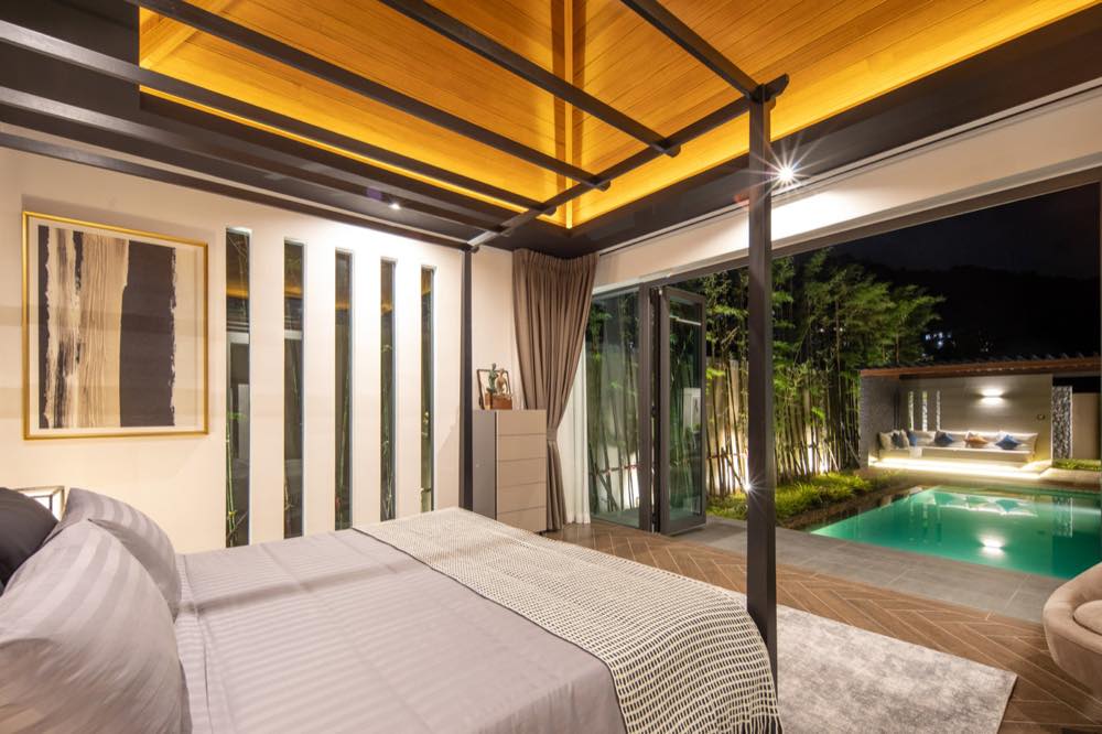 Bedroom of a pool villa in Phuket furnished by Kasa8, opening onto a lit pool at night